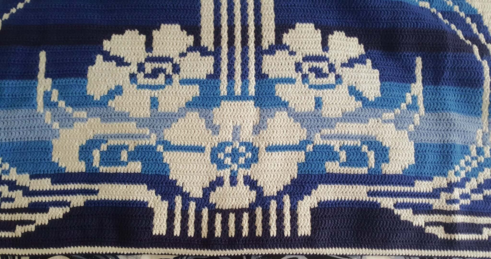 Close up of one side of the crocheted Art Nouveau Blanket showing white flowers on a blue ombre background