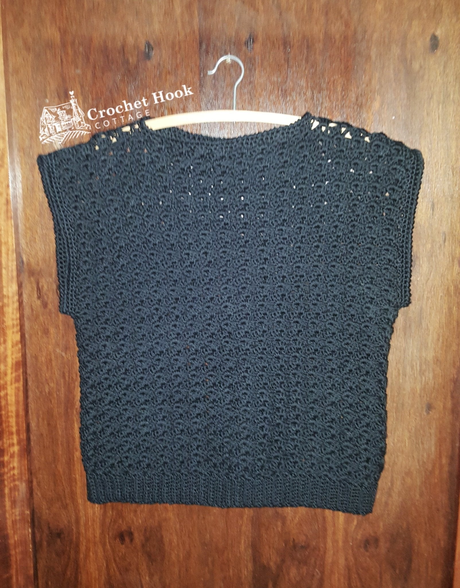 black Shell-patterned Sleeveless Ladies Top, size ladies medium, hanging on a coathanger against a wooden background - www.crochethookcottage.com