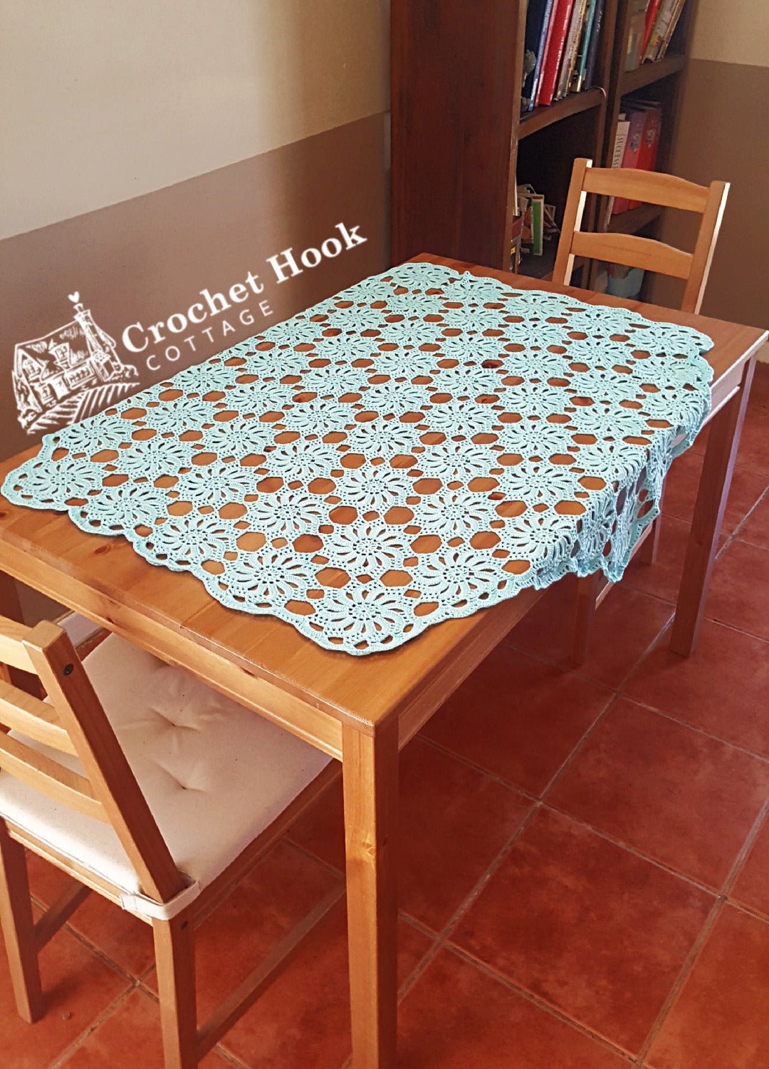 hexagonal lace crocheted Wheels of Fortune Tablecloth on a 6 seater wooden table with a chair at either end of the table and a bookcase in the background- www.crochethookcottage.com